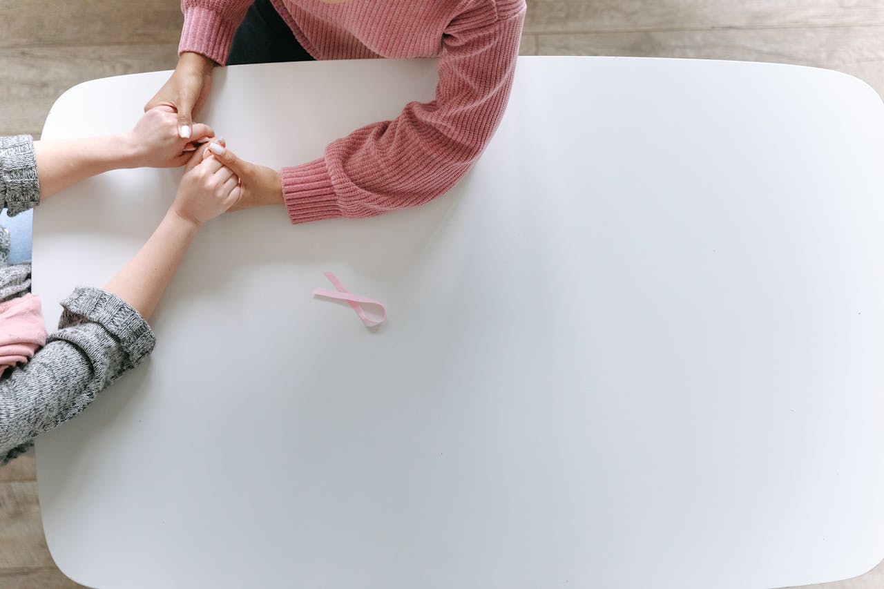 Hands holding in support with a pink ribbon symbolizing breast cancer awareness.